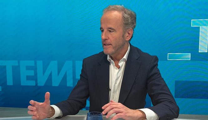 Alejandro López-Fonta, con americana azul marino y camisa blanca, explicando con un gesto de la mano, sentado a la mesa de un plató de televisión con fondo azul.