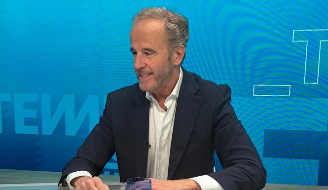 Alejandro López-Fonta, sonriente, con americana azul marino y camisa blanca, sentado a la mesa de un plató de televisión con fondo azul.