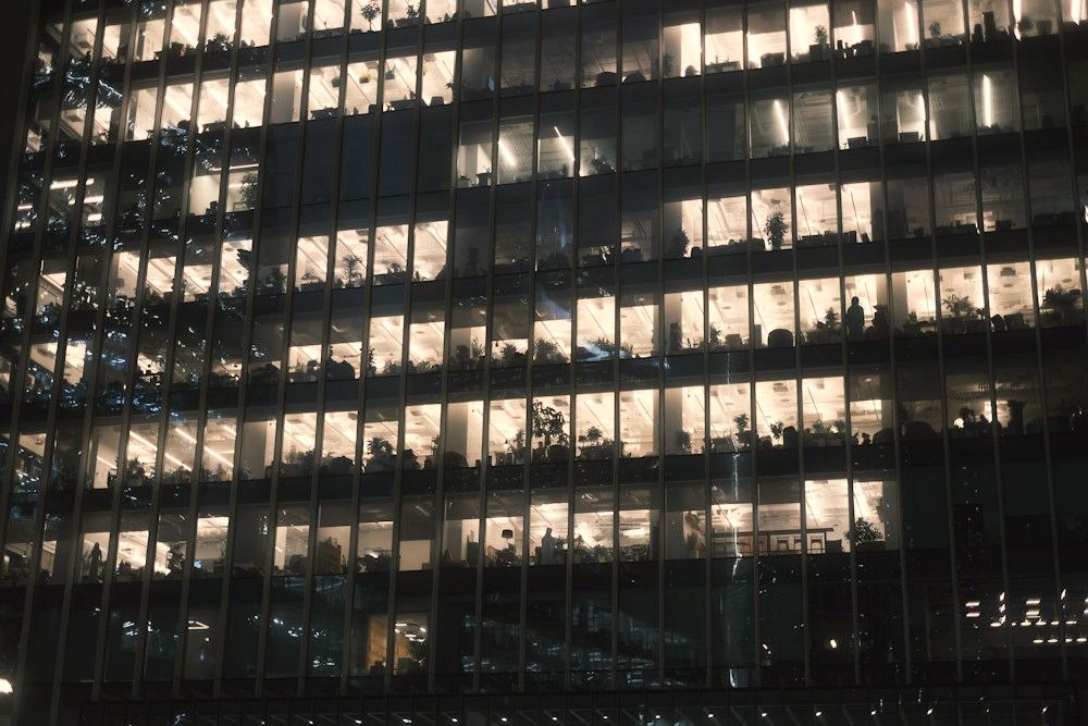 Fachada de un edificio de oficinas de noche, con las plantas iluminadas y gente trabajando tras los cristales.
